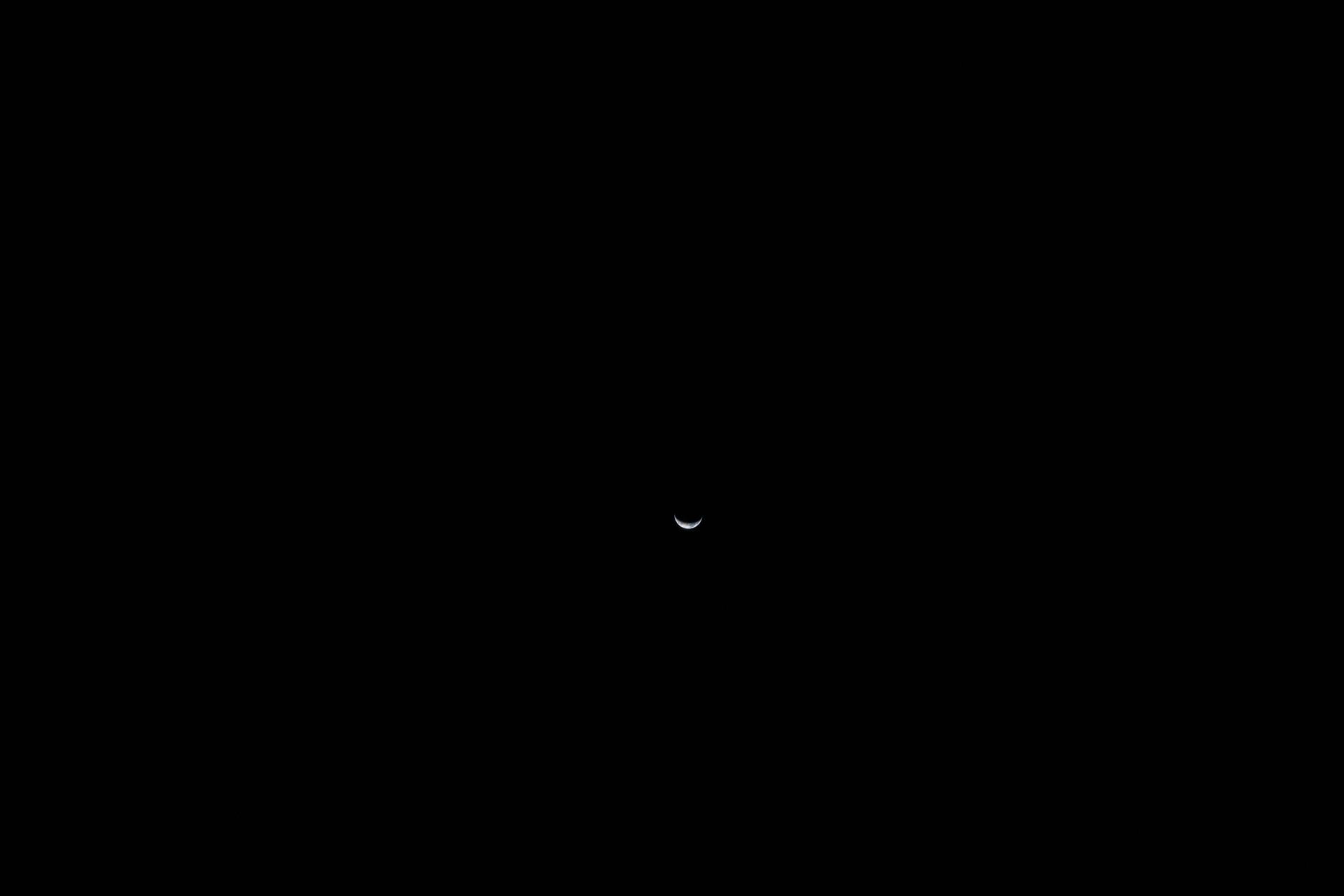 A small waning crescent Earth seen from deep space during Artemis II, faint blue tones and cloud structure visible against black space — April 6, 2026