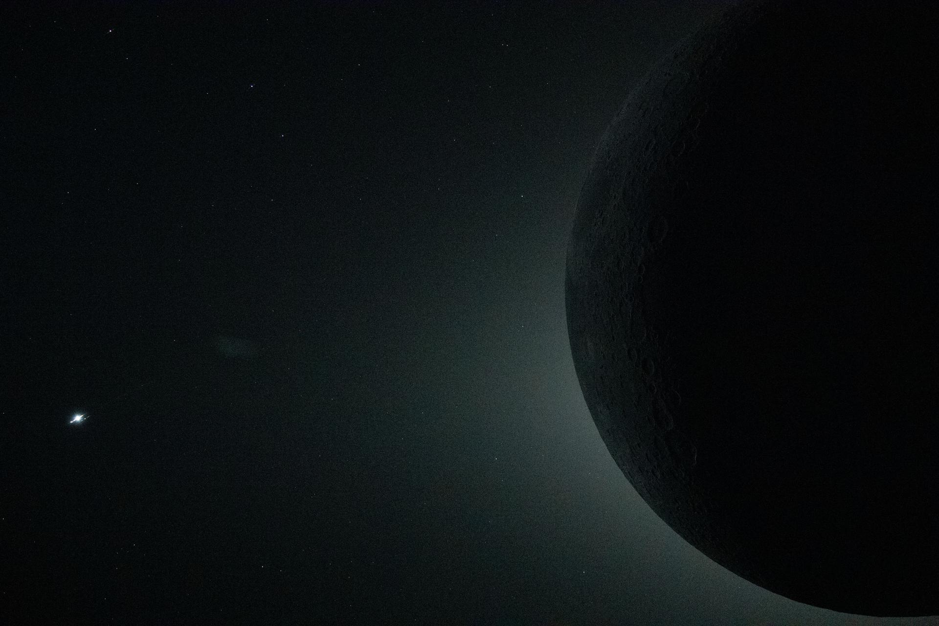Total solar eclipse viewed from inside the Orion spacecraft: the Moon fully obscures the Sun, its glowing corona visible around the dark lunar disk, with Venus as a bright point of light at upper left — April 6, 2026